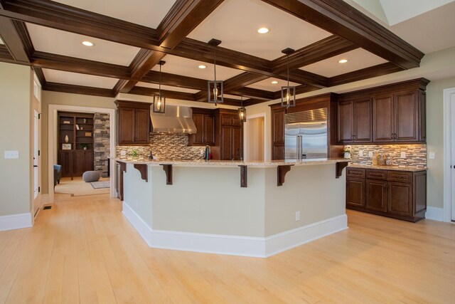 kitchen with built in fridge, decorative light fixtures, a kitchen breakfast bar, a large island, and wall chimney range hood