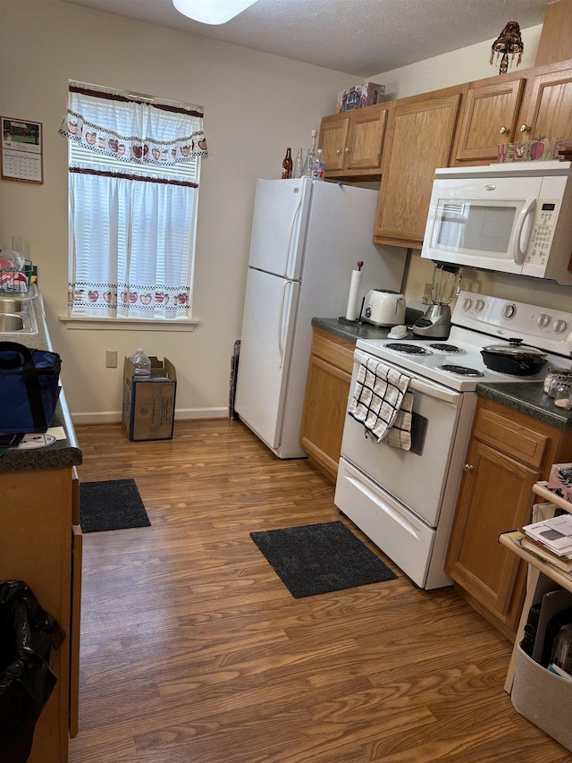 kitchen featuring white appliances, dark countertops, and wood finished floors