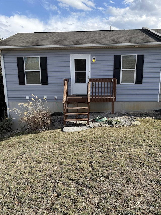 view of front facade with a front lawn, roof with shingles, and a wooden deck