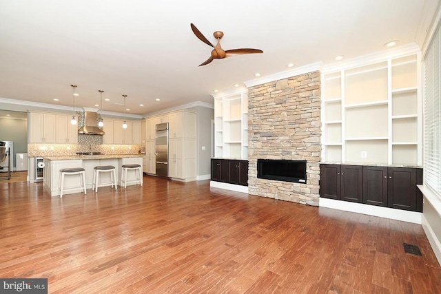 unfurnished living room with a fireplace, wine cooler, ceiling fan, crown molding, and light hardwood / wood-style flooring