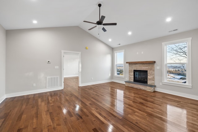 unfurnished living room featuring ceiling fan, a stone fireplace, a healthy amount of sunlight, and dark hardwood / wood-style flooring