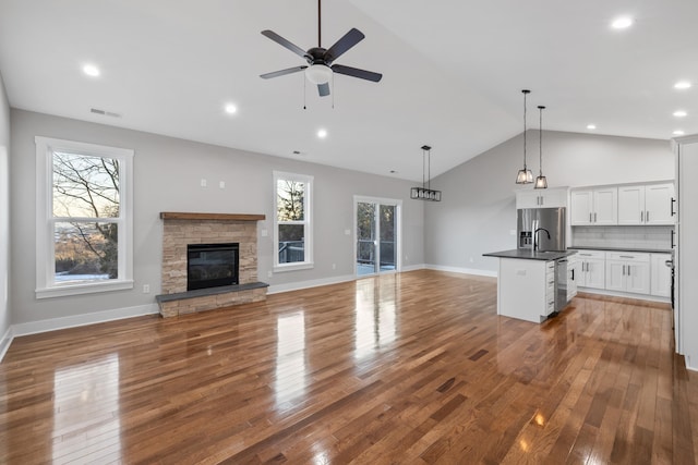 unfurnished living room with vaulted ceiling, a fireplace, sink, hardwood / wood-style flooring, and ceiling fan