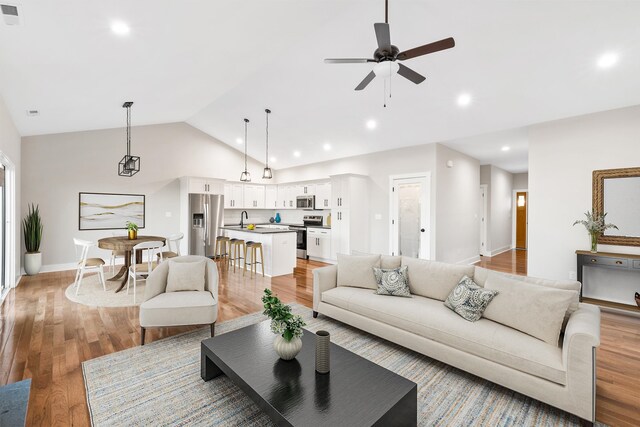 living room with sink, vaulted ceiling, ceiling fan, and light wood-type flooring