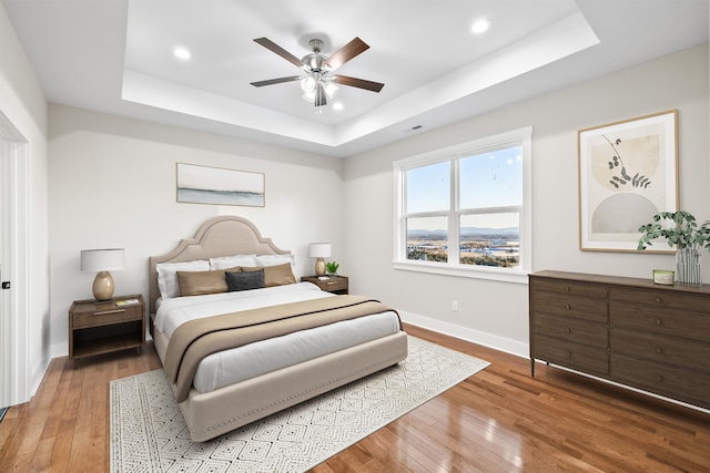 bedroom with hardwood / wood-style floors, ceiling fan, and a tray ceiling