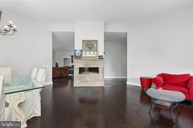 living area featuring a notable chandelier, a lit fireplace, baseboards, and wood finished floors