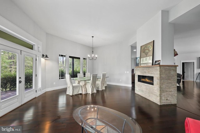 dining space featuring a notable chandelier, a stone fireplace, baseboards, and wood finished floors