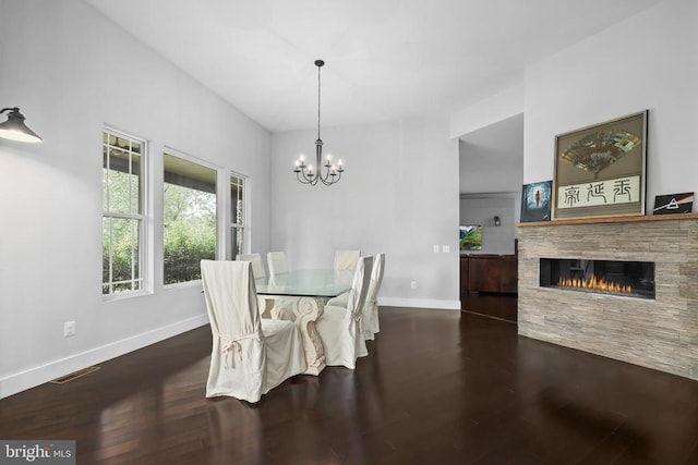 dining space with visible vents, a stone fireplace, wood finished floors, a chandelier, and baseboards