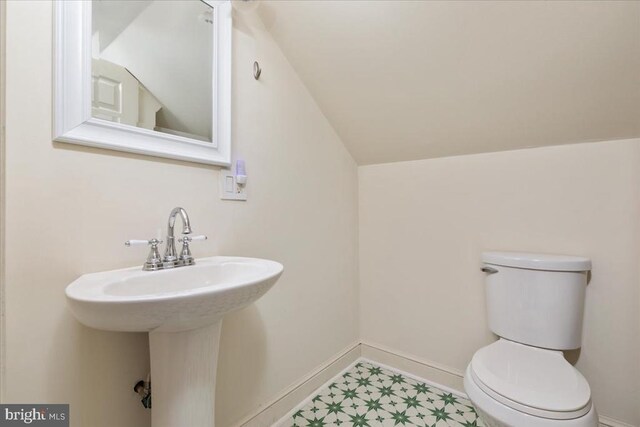 half bathroom featuring baseboards, tile patterned floors, vaulted ceiling, and toilet
