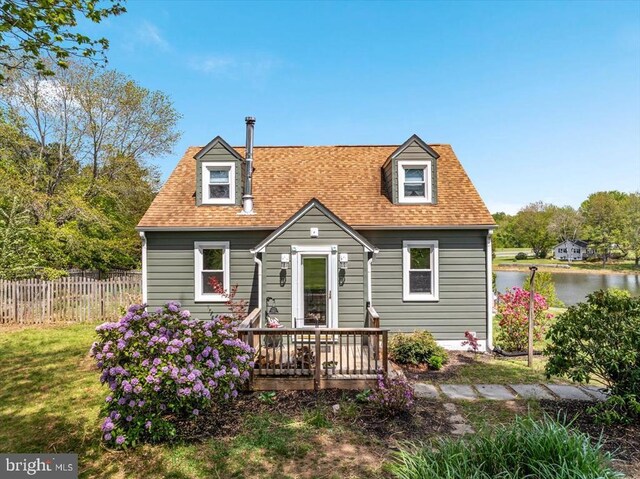 new england style home featuring fence, a water view, a front lawn, and roof with shingles