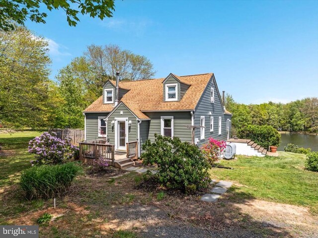 new england style home featuring roof with shingles, a water view, and a front yard