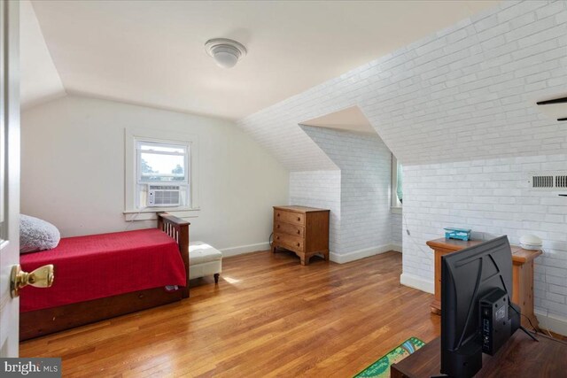 bedroom featuring brick wall, wood finished floors, baseboards, cooling unit, and lofted ceiling
