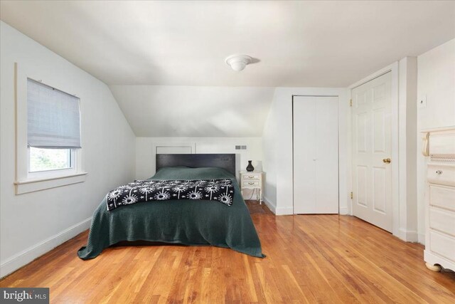 bedroom featuring visible vents, a closet, lofted ceiling, wood finished floors, and baseboards