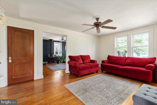 living area featuring ceiling fan, a wood stove, and wood finished floors