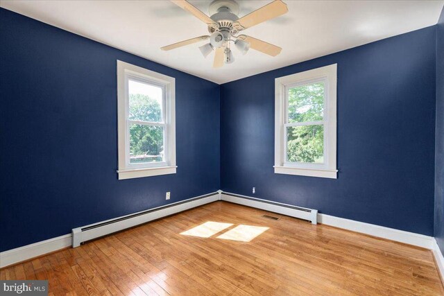 empty room featuring a baseboard heating unit, a healthy amount of sunlight, and hardwood / wood-style floors