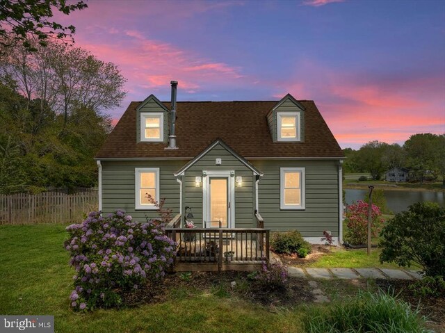cape cod-style house with fence, a shingled roof, a deck with water view, and a front yard