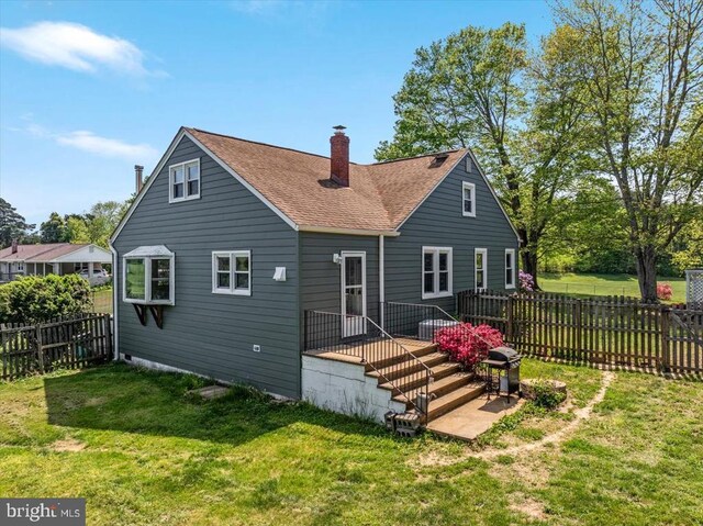 back of house with a fenced backyard, a chimney, a lawn, and roof with shingles
