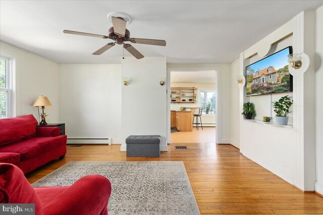 living area featuring ceiling fan, a wealth of natural light, baseboard heating, and wood finished floors
