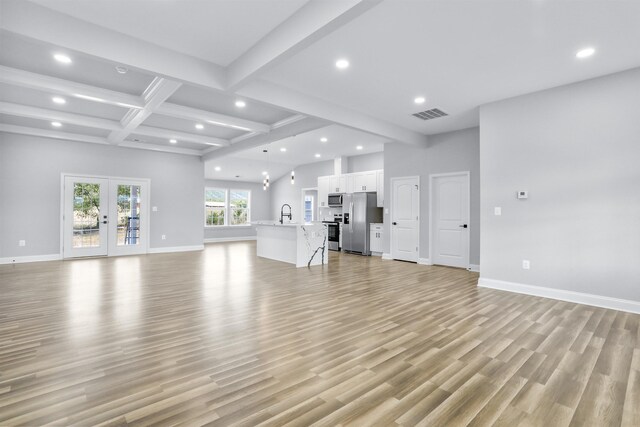 unfurnished living room with coffered ceiling, light hardwood / wood-style flooring, french doors, and beamed ceiling