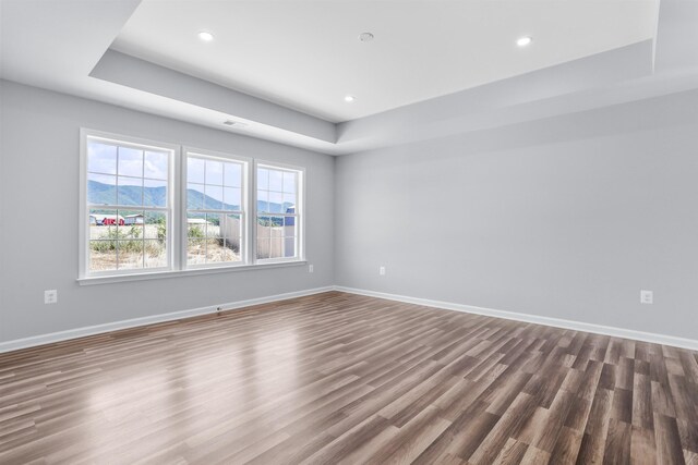 unfurnished room featuring hardwood / wood-style flooring, a tray ceiling, and a mountain view