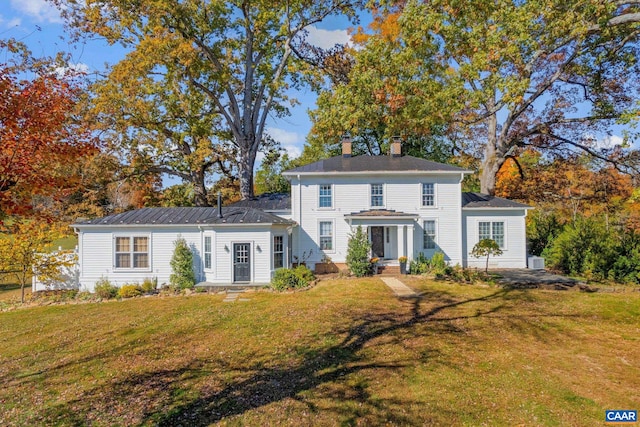 colonial-style house featuring a chimney and a front lawn