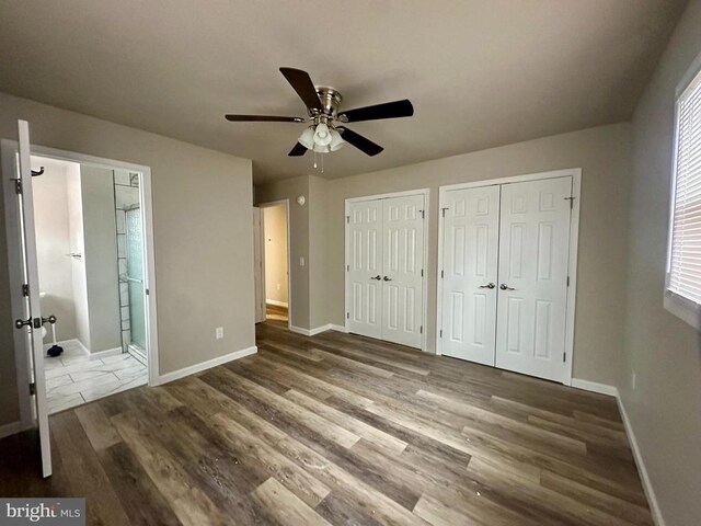 unfurnished bedroom featuring two closets, wood-type flooring, ensuite bath, and ceiling fan