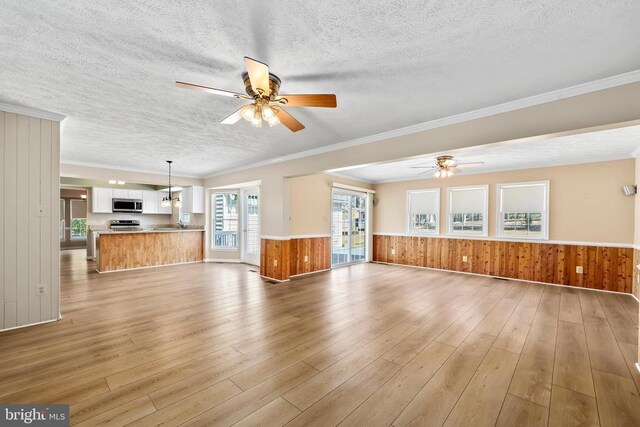 unfurnished living room featuring a wainscoted wall, a ceiling fan, light wood-type flooring, and a textured ceiling