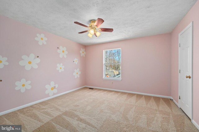 carpeted spare room with visible vents, a ceiling fan, baseboards, and a textured ceiling