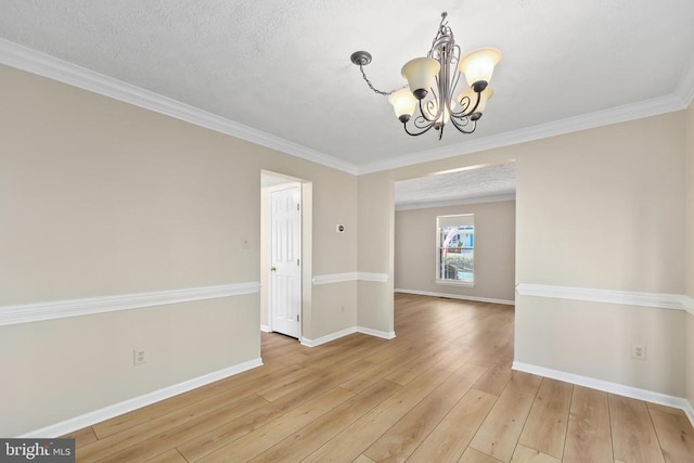 spare room with a textured ceiling, light wood-style floors, an inviting chandelier, crown molding, and baseboards