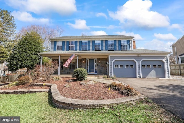 view of front facade with driveway, stone siding, a porch, fence, and a garage