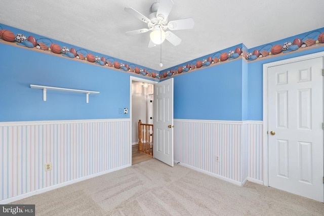 carpeted spare room featuring a wainscoted wall and ceiling fan