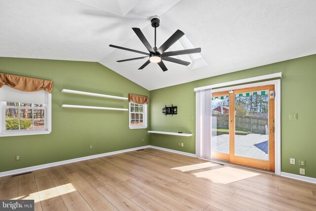 spare room featuring a ceiling fan, wood finished floors, visible vents, baseboards, and vaulted ceiling with skylight