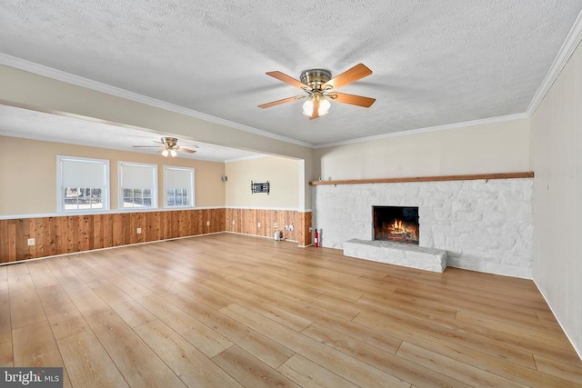 unfurnished living room with a wainscoted wall, a warm lit fireplace, a textured ceiling, and hardwood / wood-style floors