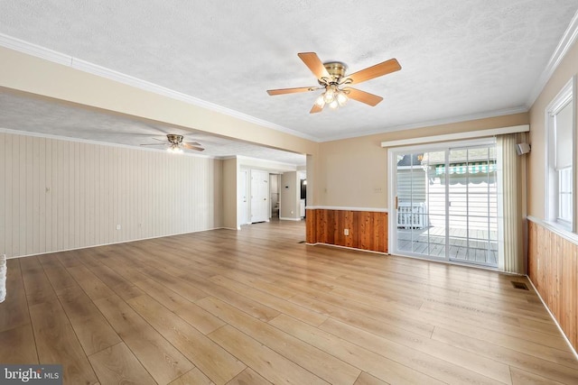 unfurnished living room with crown molding, wooden walls, light wood finished floors, and a textured ceiling