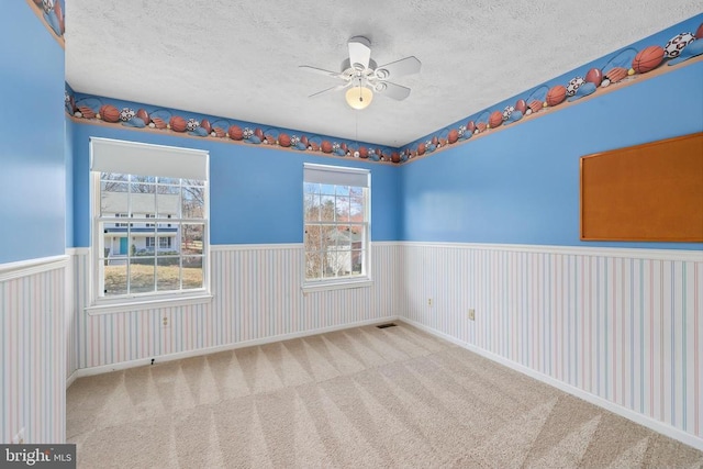 carpeted spare room with ceiling fan, a wainscoted wall, and a textured ceiling