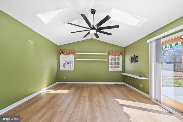 empty room featuring vaulted ceiling with skylight, ceiling fan, baseboards, and wood finished floors