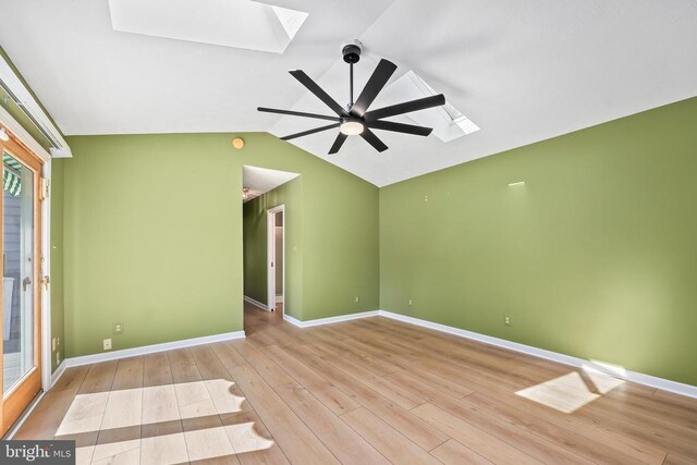 empty room with baseboards, lofted ceiling with skylight, wood finished floors, and a ceiling fan