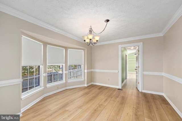 spare room with a notable chandelier, ornamental molding, a textured ceiling, light wood finished floors, and baseboards