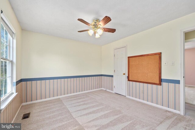 carpeted spare room with a wainscoted wall, visible vents, ceiling fan, and wallpapered walls