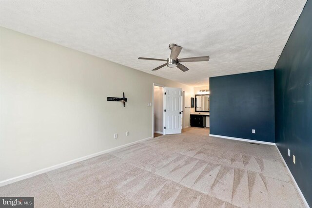 unfurnished bedroom featuring light colored carpet, a textured ceiling, connected bathroom, and baseboards