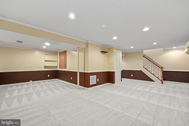 finished below grade area featuring stairway, carpet floors, visible vents, and ornamental molding