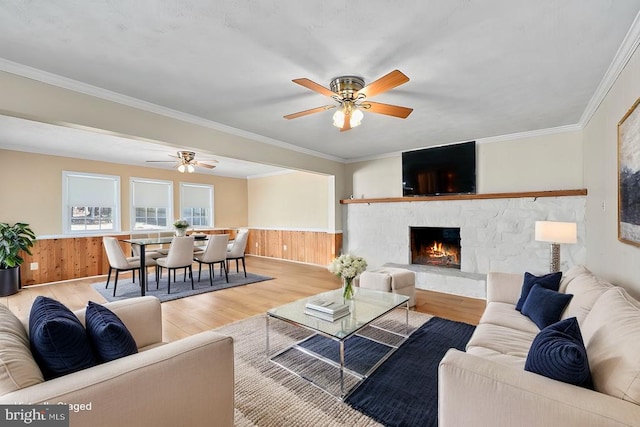 living room featuring wainscoting, a stone fireplace, ornamental molding, and wood finished floors