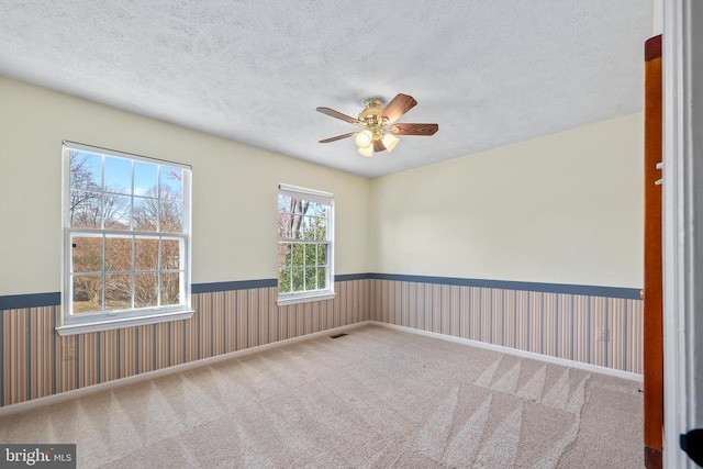 spare room with wainscoting, a textured ceiling, a ceiling fan, and carpet floors