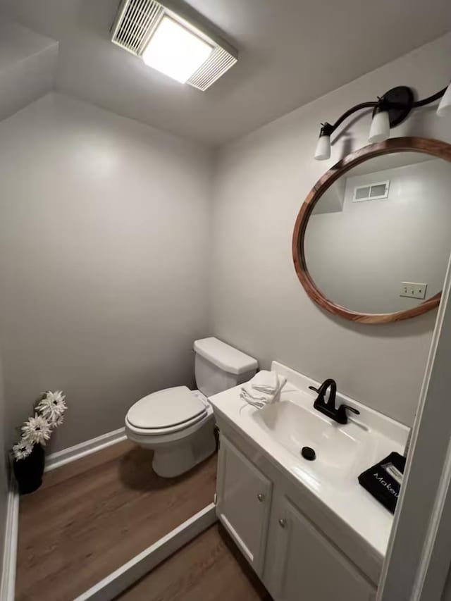 bathroom with wood finished floors, vanity, baseboards, toilet, and visible vents
