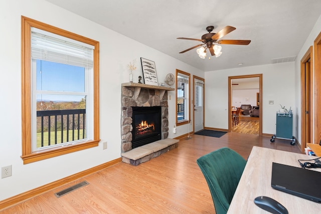 living room with ceiling fan, a stone fireplace, and hardwood / wood-style floors