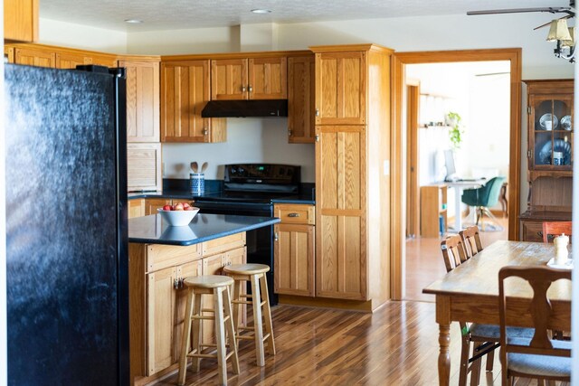 kitchen with hardwood / wood-style flooring, a kitchen bar, and black appliances