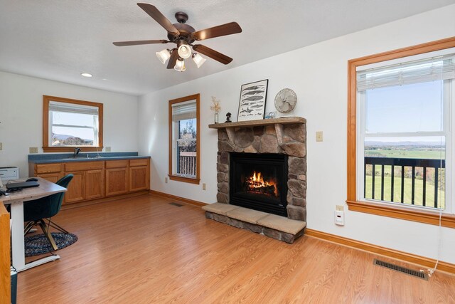 office space featuring ceiling fan, a stone fireplace, sink, and light wood-type flooring