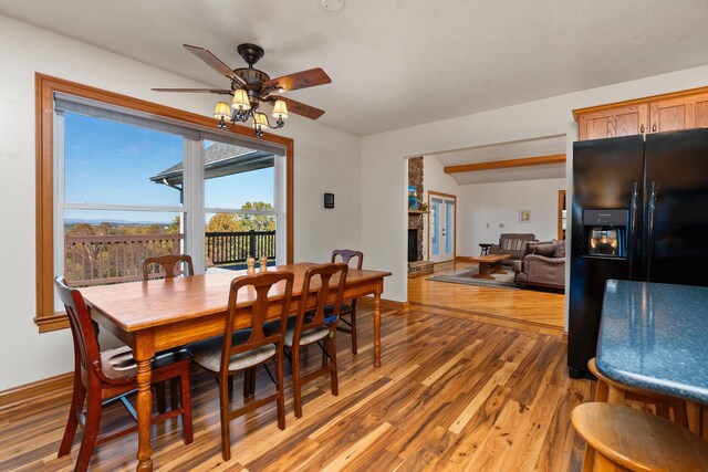 dining space featuring hardwood / wood-style flooring, a large fireplace, and ceiling fan