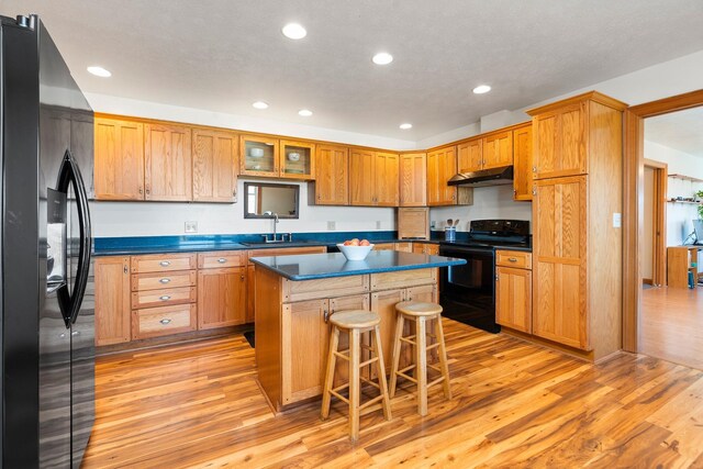 kitchen with sink, a breakfast bar area, black appliances, light hardwood / wood-style floors, and a kitchen island