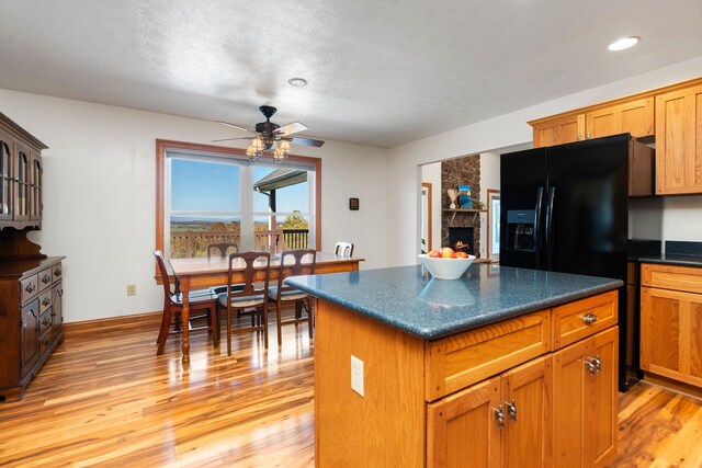 kitchen featuring a fireplace, a center island, black fridge with ice dispenser, ceiling fan, and light hardwood / wood-style flooring