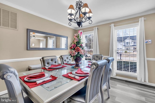 dining space with an inviting chandelier, ornamental molding, and light wood-type flooring